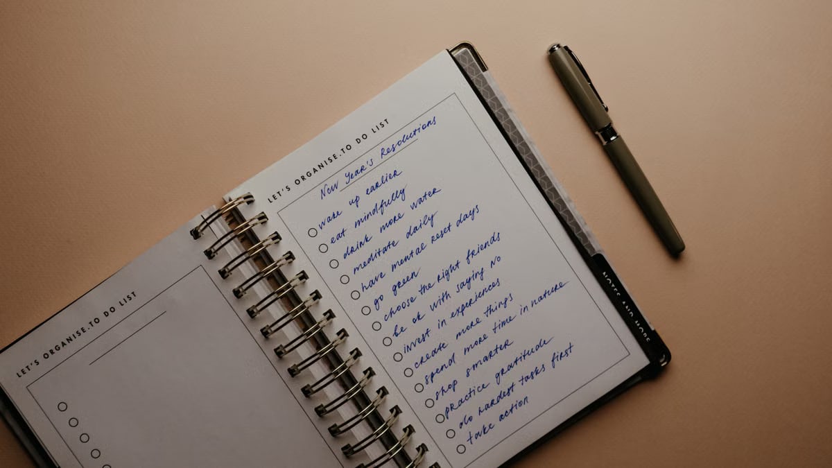 An open notebook on a brown background featuring handwritten New Year's resolutions.